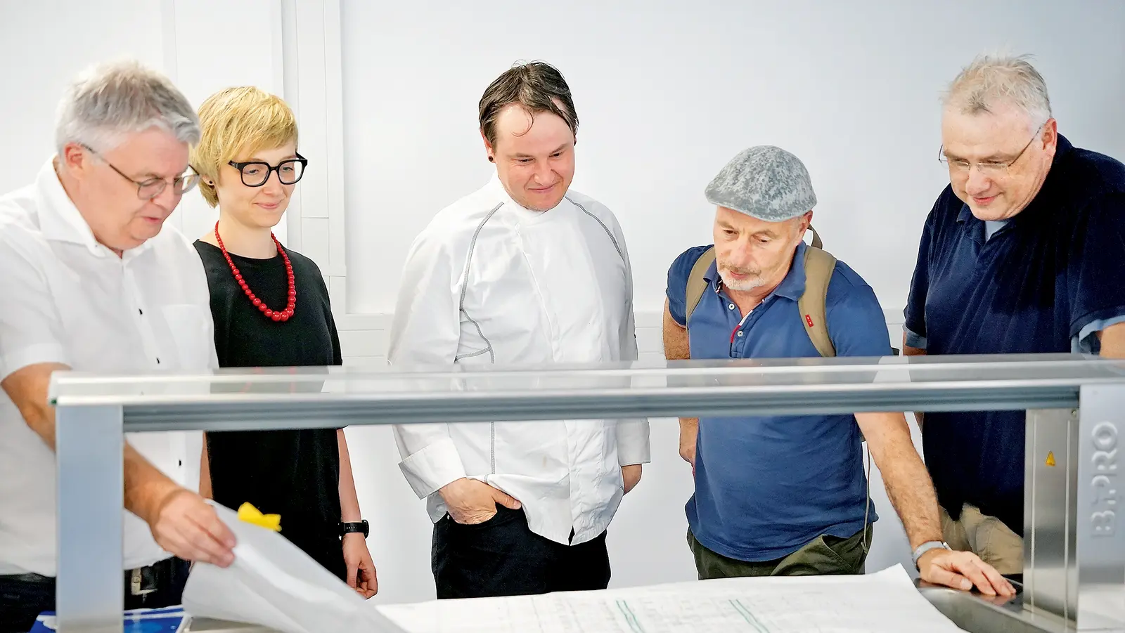 Fünf Personen begutachten gemeinsam Baupläne und besprechen ein laufendes Bauprojekt.