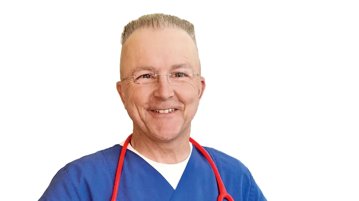 Porträt von Dr. Christian Falkenberg im blauen Kasack mit rotem Stethoskop um den Hals vor weißem Hintergrund.