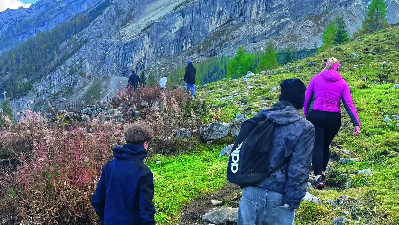 Drei Wanderer auf einem Pfad in bergiger Landschaft unter bewölktem Himmel