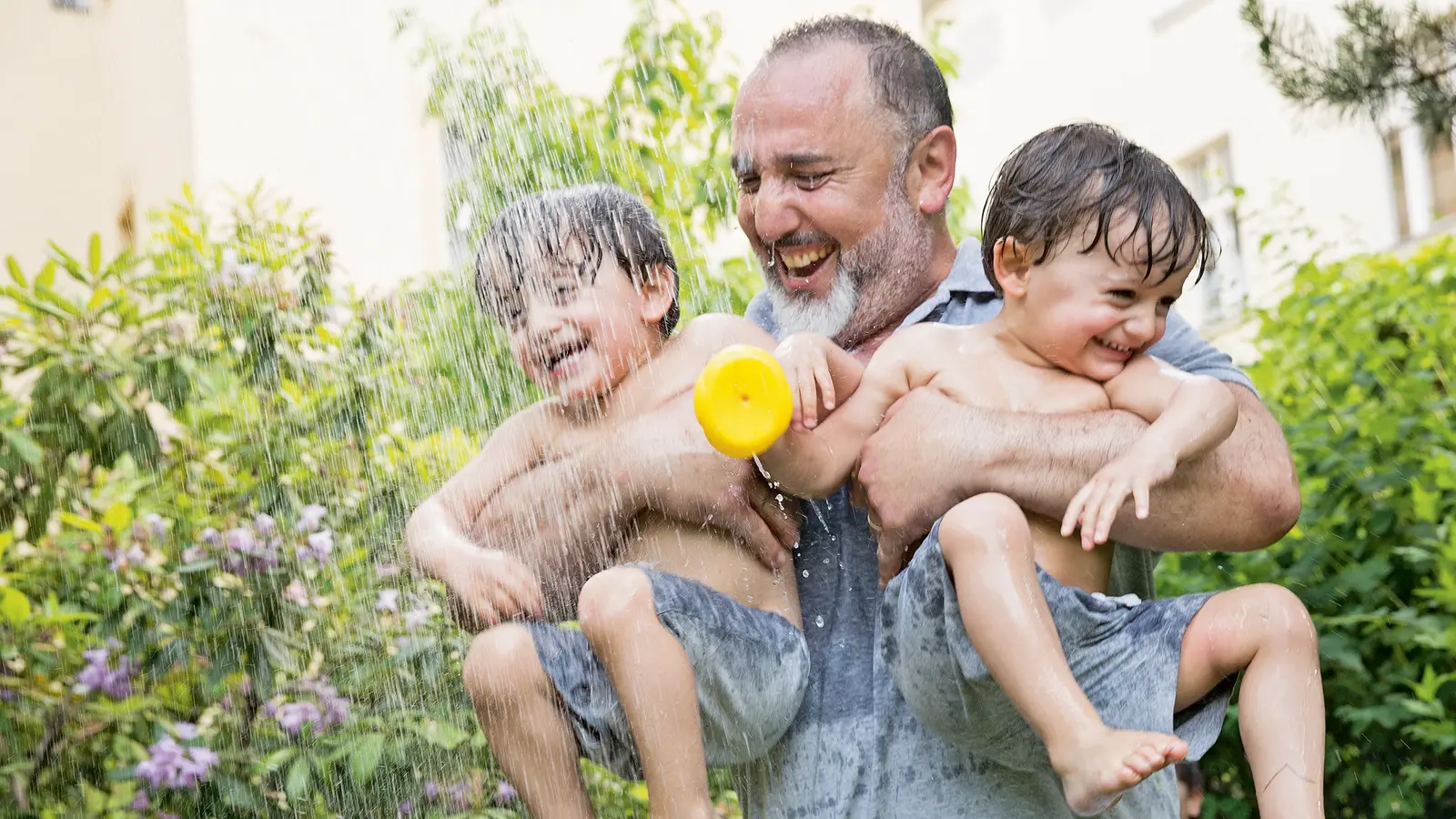 Ein Vater spielt lachend mit seinen zwei Kindern unter Wasser.