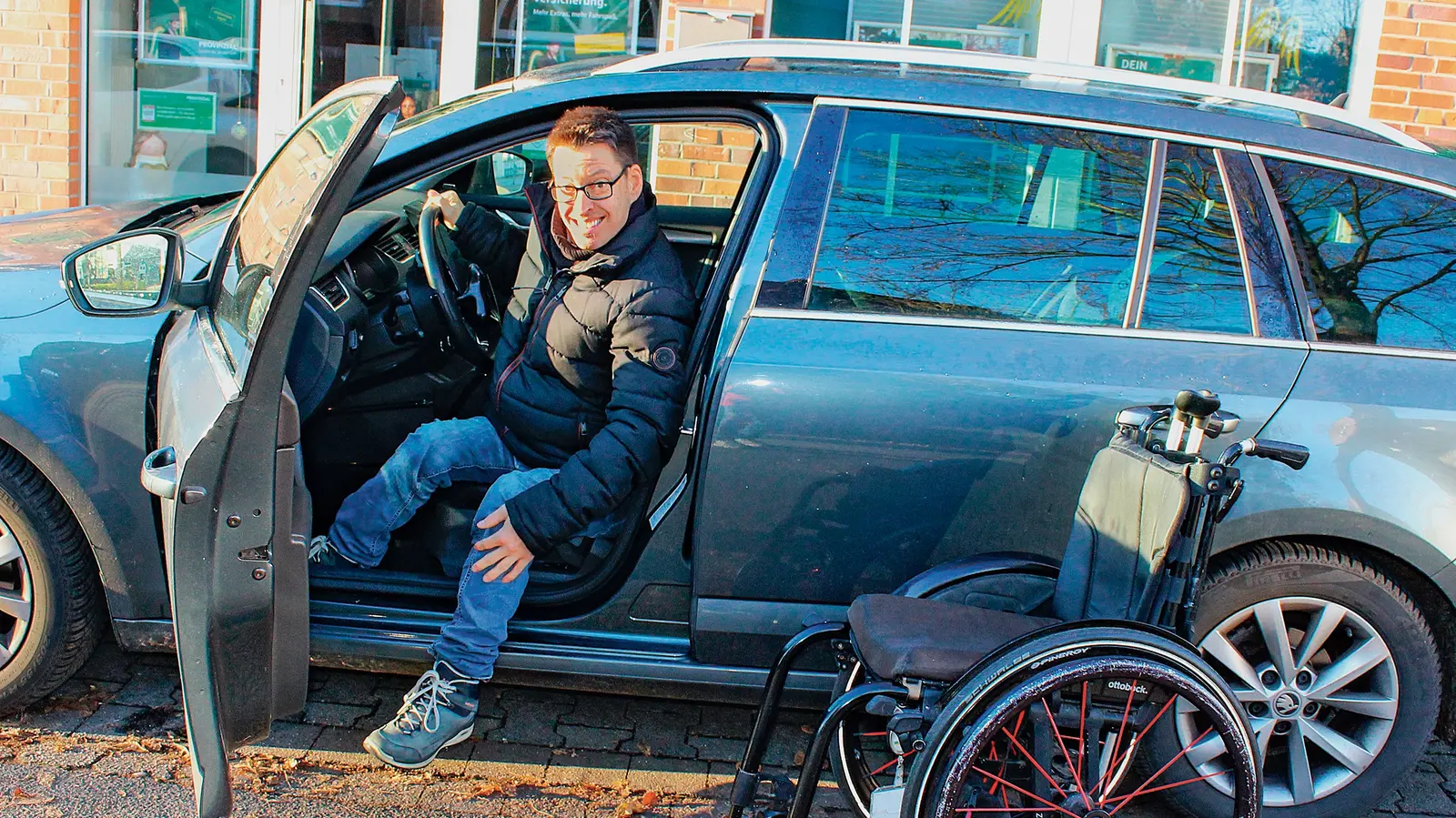Ein Mann im Auto mit geöffneter Tür in die Kamera blickend.