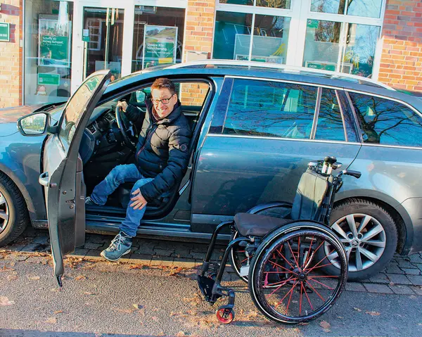 Ein Mann im Auto mit geöffneter Tür in die Kamera blickend.