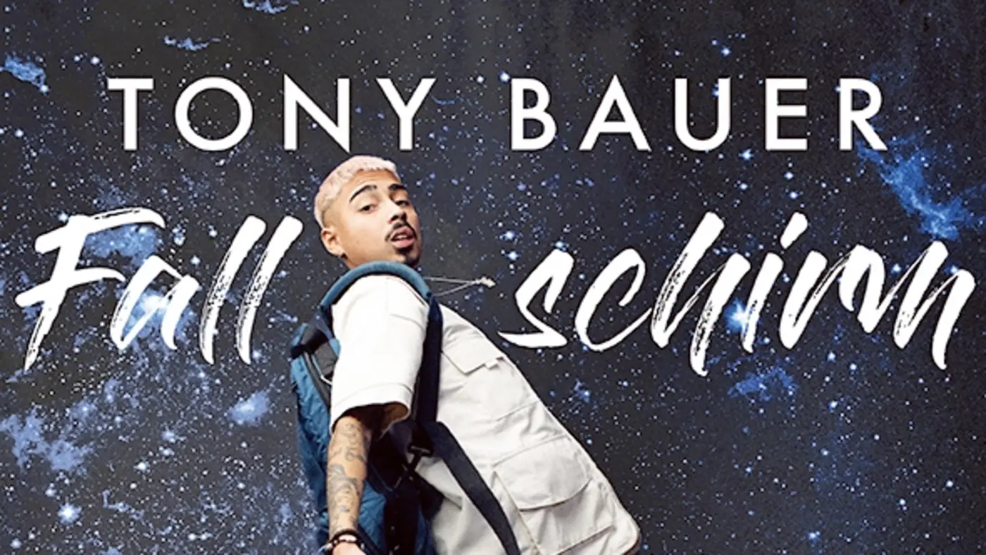 Plakatmotiv der Live-Tour von Comedian Tony Bauer. Vor einem galaktischen Hintergrund mit Sternen ist Tony Bauer in einem hellen Outfit mit Fallschirm-Rucksack zu sehen, als würde er durch den Weltraum springen oder fallen. Über ihm steht in großen Buchstaben sein Name: ‚Tony Bauer‘. Darunter der Tourtitel: ‚Fallschirm Springer‘ in dynamischer, handschriftartiger Schrift. Unten im Bild stehen die Worte ‚Live Tour‘ sowie Social-Media-Icons, eine Website-Adresse (tonybauer.de) und ein QR-Code für Tickets