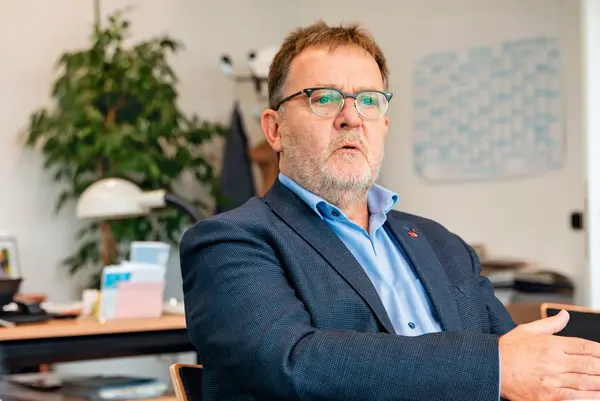 Porträt von Dieter Hillebrand mit Brille, dunklem Sakko und blauem Hemd im Gespräch in einem Büro.