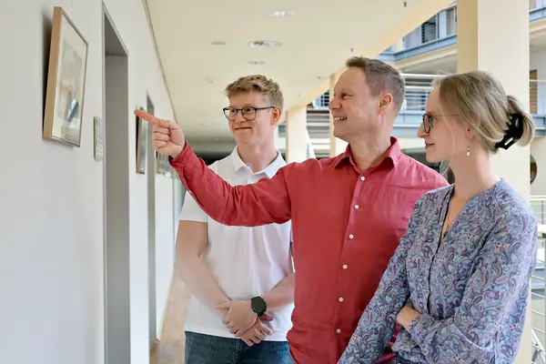 Ein Vater zeigt seinen zwei Kindern ein Foto an der Wand.