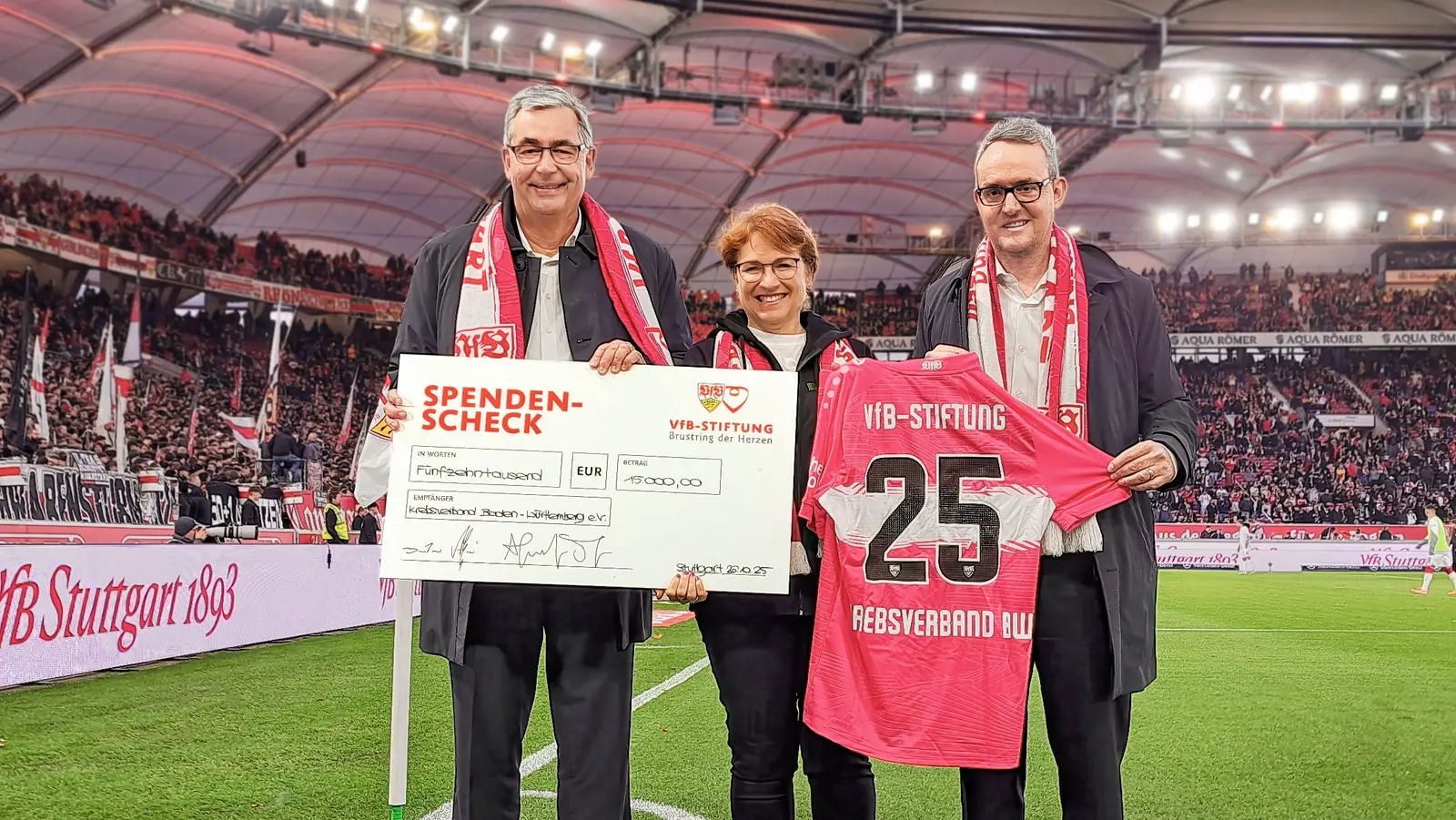 Drei Personen stehen im Stadion auf dem Feld und halten einen Spendencheck in der Hand.