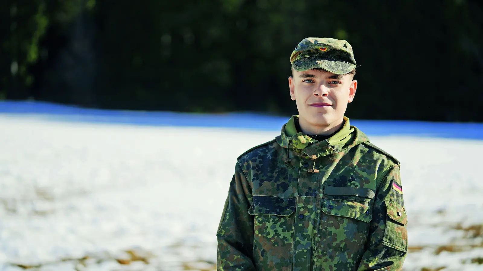 Ein junger Mann in Militäruniform blickt lächelnd in die Kamera.