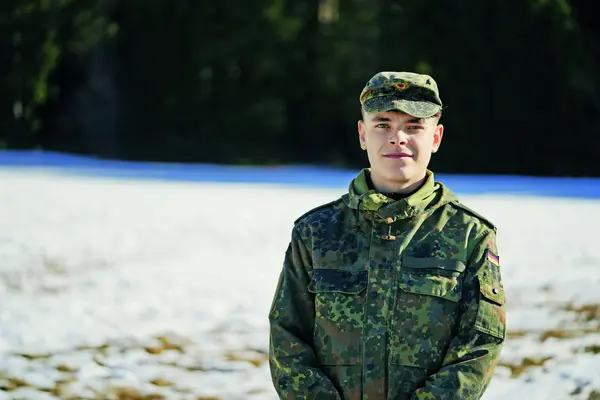 Ein junger Mann in Militäruniform blickt lächelnd in die Kamera.