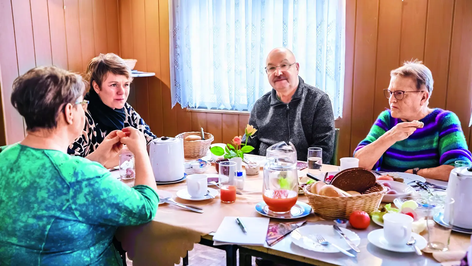 Vier ältere Personen, die gemeinsam an einem Tisch sitzen und frühstücken.