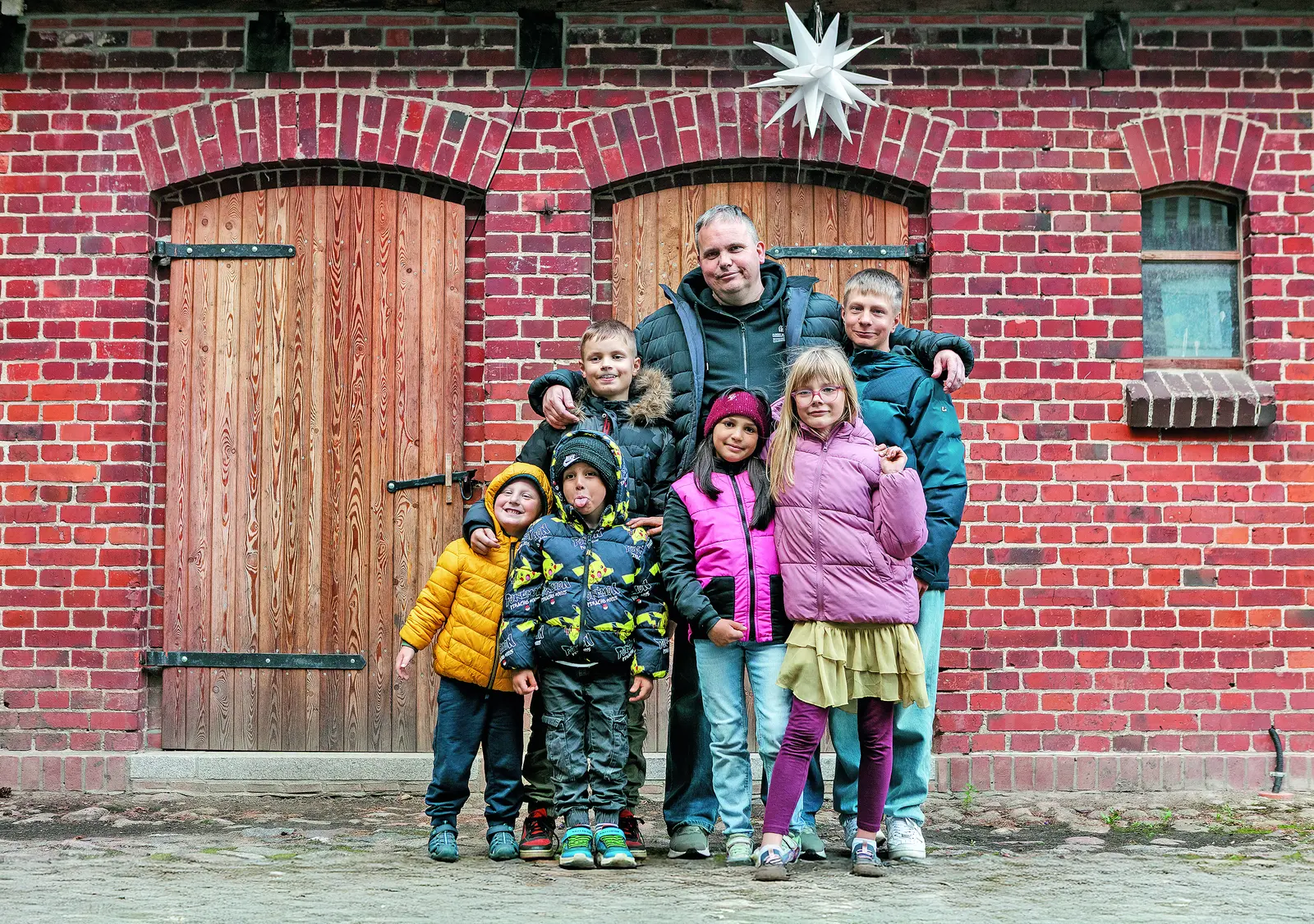 Gruppenfoto: Ein Mann und mehrere Kinder stehen vor einem Häuschen.