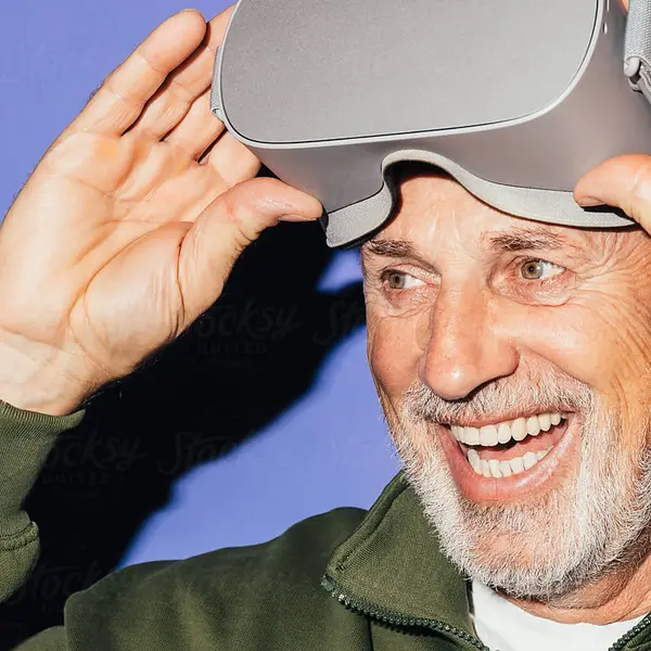 Nahaufnahme eines älteren Mannes, der lächelt und gerade eine Virtual‑Reality‑Brille anhebt; das Bild zeigt seine begeisterte Mimik beim VR‑Erlebnis.