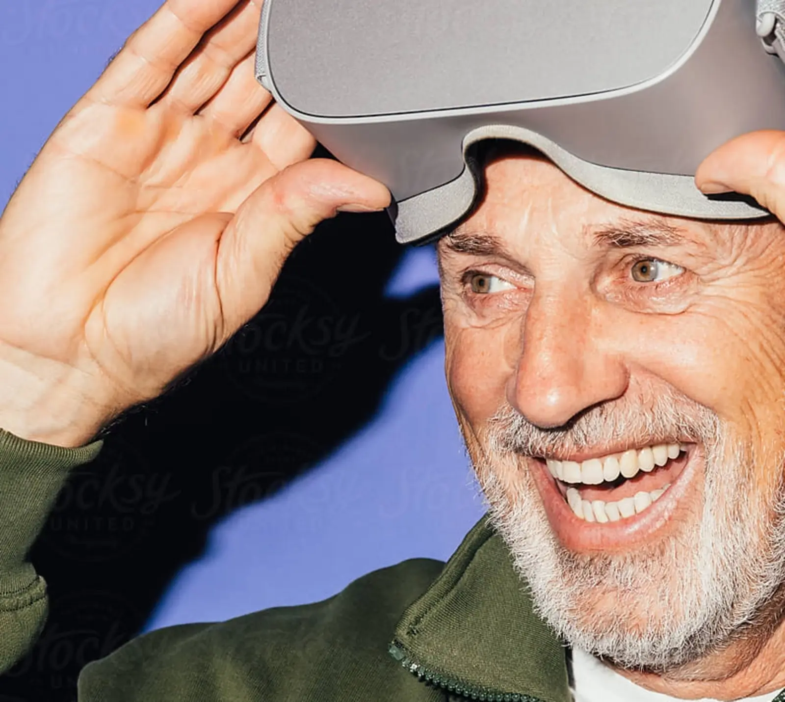 Nahaufnahme eines älteren Mannes, der lächelt und gerade eine Virtual‑Reality‑Brille anhebt; das Bild zeigt seine begeisterte Mimik beim VR‑Erlebnis.