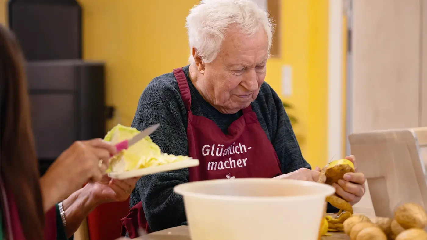 Ein älterer Mann sitzt am Tisch und schält Kartoffeln.