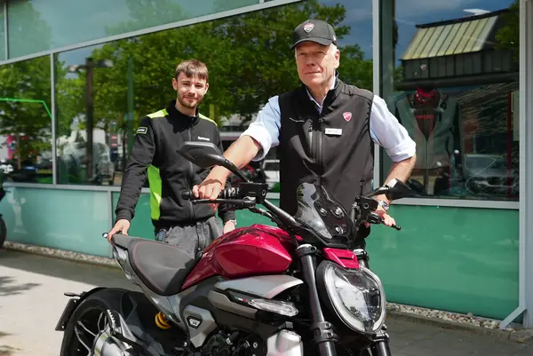 Ein älterer Herr hält ein Motorrad vor sich und neben ihm steht ein junger Mann.