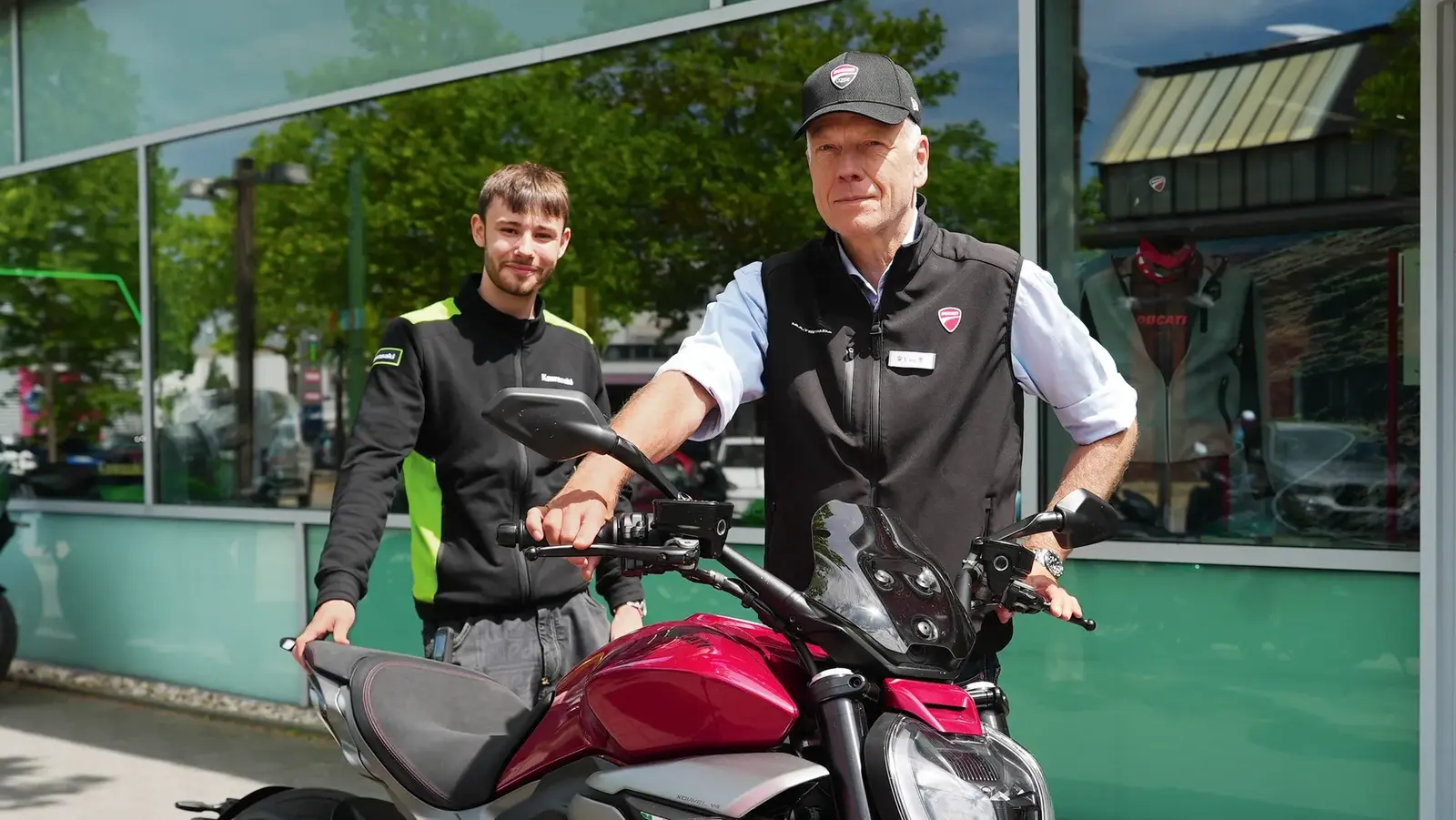Ein älterer Herr hält ein Motorrad vor sich und neben ihm steht ein junger Mann.