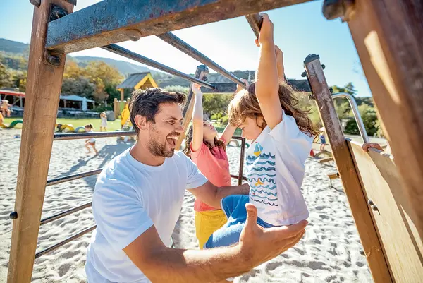 Ein Mann spielt voller Freude mit seinem Kind am Spielplatz.