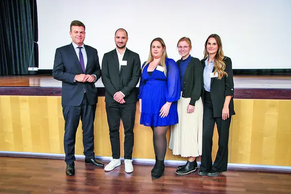 Fünf Personen stehen auf einer Ehrungsbühne blickend in die Kamera. 