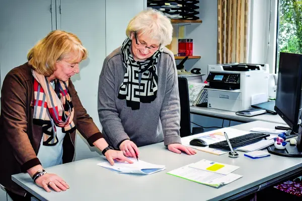 Zwei ältere Frauen sind in einem Büro an einem Schreibtisch und betrachten gemeinsam Unterlagen.