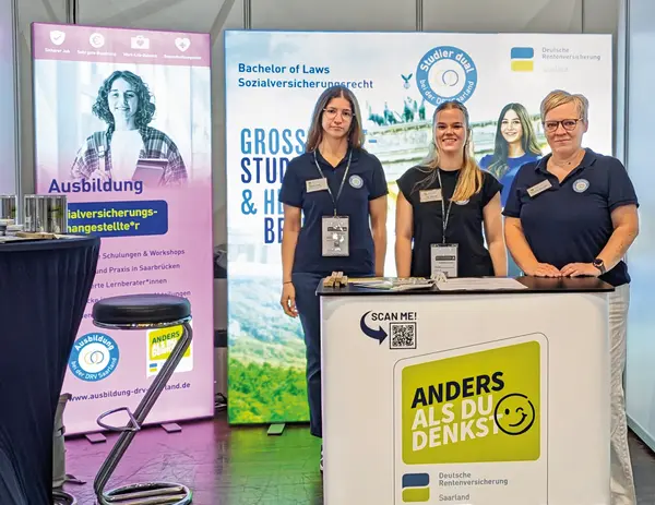 Drei Damen befinden sich auf einer Messe und stehen hinter einem Stand.