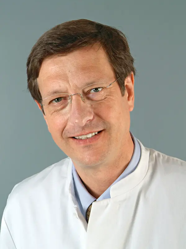 Porträt von Prof. Dr. Josef Rosenecker mit Brille und weißem Arztkittel vor grauem Hintergrund.