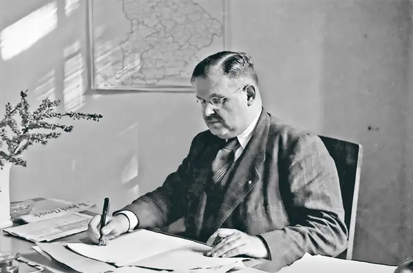 Philipp Auerbach verfasst am Schreibtisch etwas auf Blatt Papier.