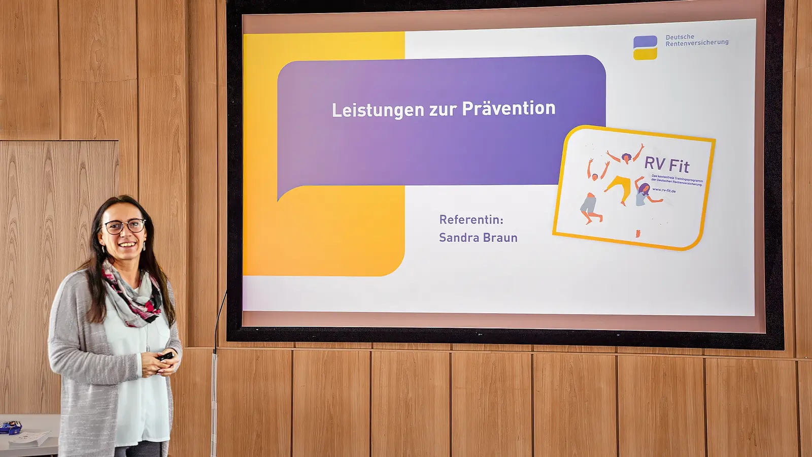 Eine Frau hält eine Präsentation mit einem großen Bildschirm hinter ihr. 