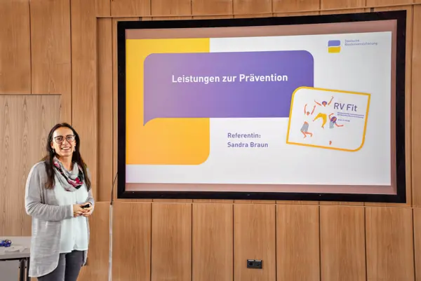 Eine Frau hält eine Präsentation mit einem großen Bildschirm hinter ihr. 