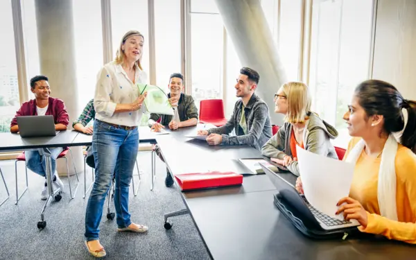 Eine Dozentin erklärt einer Gruppe Studierender etwas in einem Seminarraum.