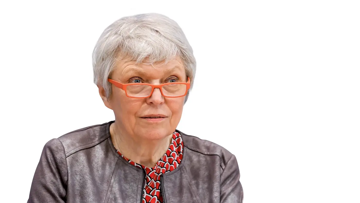 Porträt von Doris Barnett mit kurzen grauen Haaren und auffälliger orangefarbener Brille.