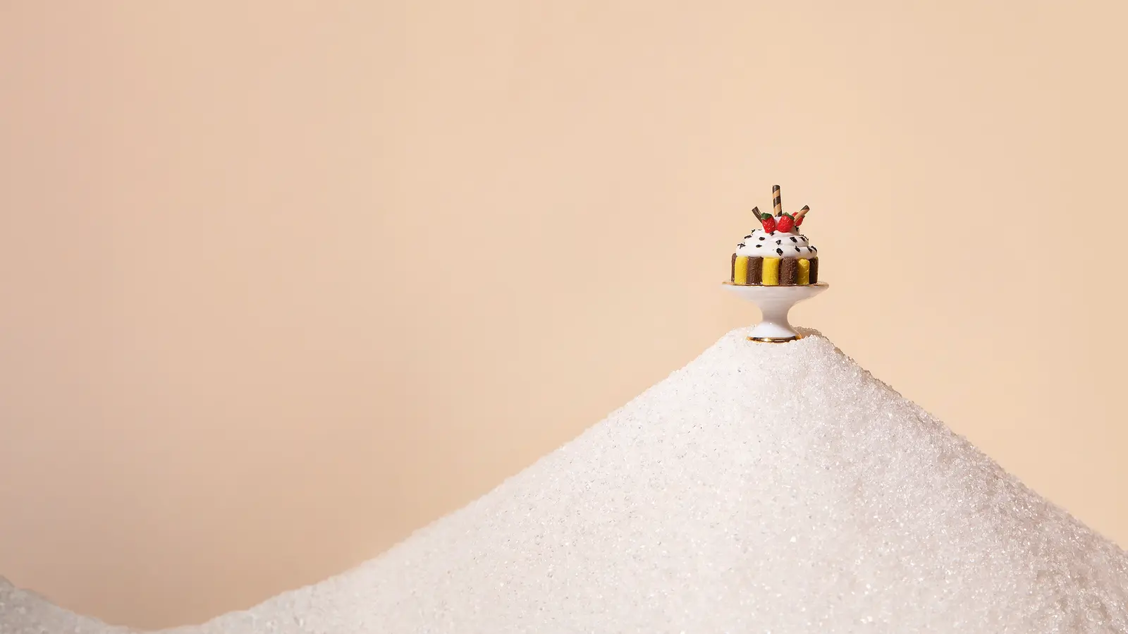 Ein kleiner Kuchen steht auf einem großen Berg aus Zucker vor hellem, minimalistischem Hintergrund.