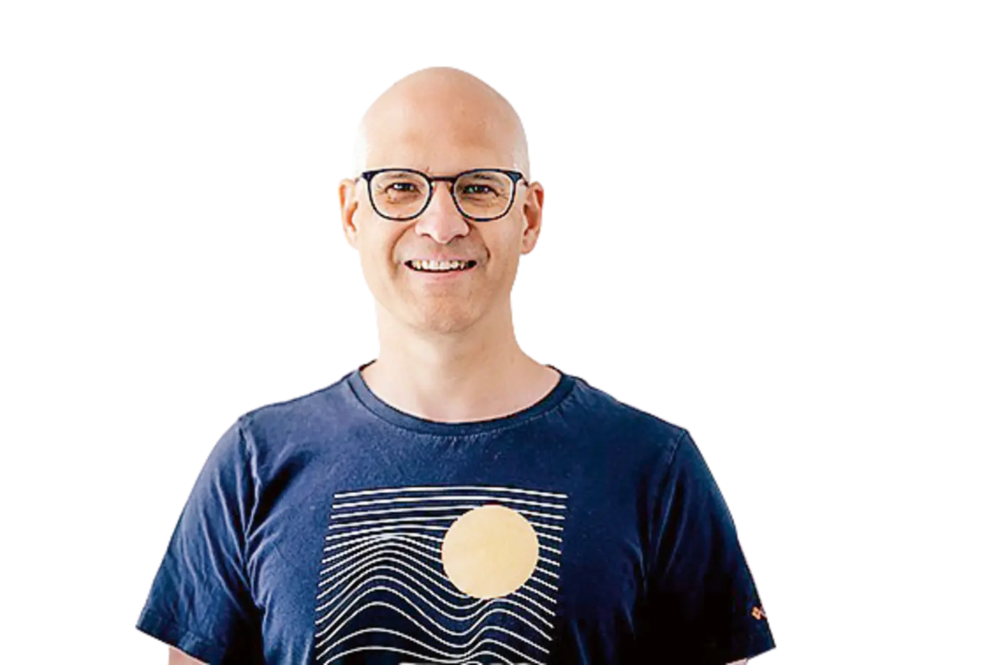 Das Bild zeigt einen lächelnden Mann mit kahlem Kopf, der eine Brille trägt und ein dunkelblaues T-Shirt mit einem grafischen Design von einer Sonne und Wellen trägt. Im Hintergrund ist ein rotes Luftballon sichtbar. Er wirkt freundlich und entspannt.