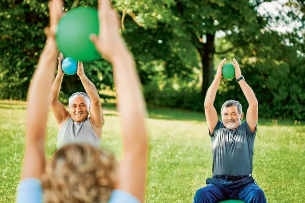 Zwei ältere Männer machen im Freien Gymnastikübungen mit kleinen Bällen
