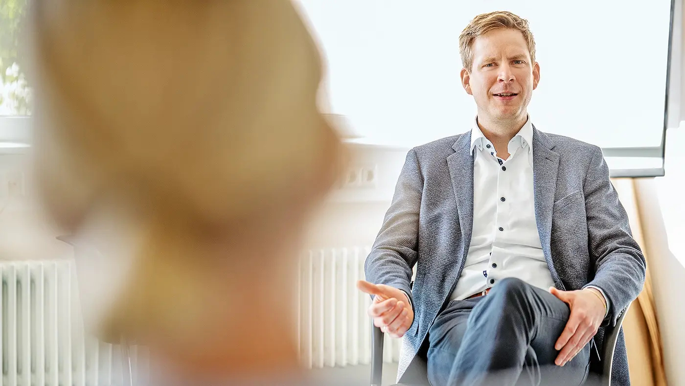 Ein Mann sitzt auf dem Stuhl und redet dabei mit einer anderen Person.