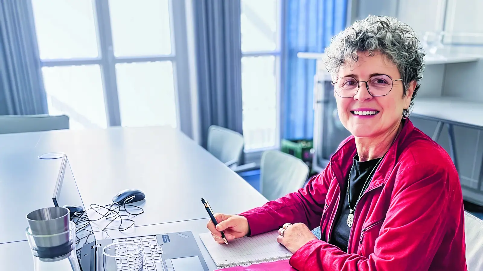 Eine Dame sitzt mit einem Laptop und einem Notizbuch am Tisch. 