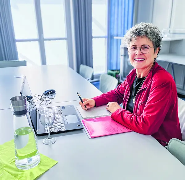 Eine Dame sitzt mit einem Laptop und einem Notizbuch am Tisch. 